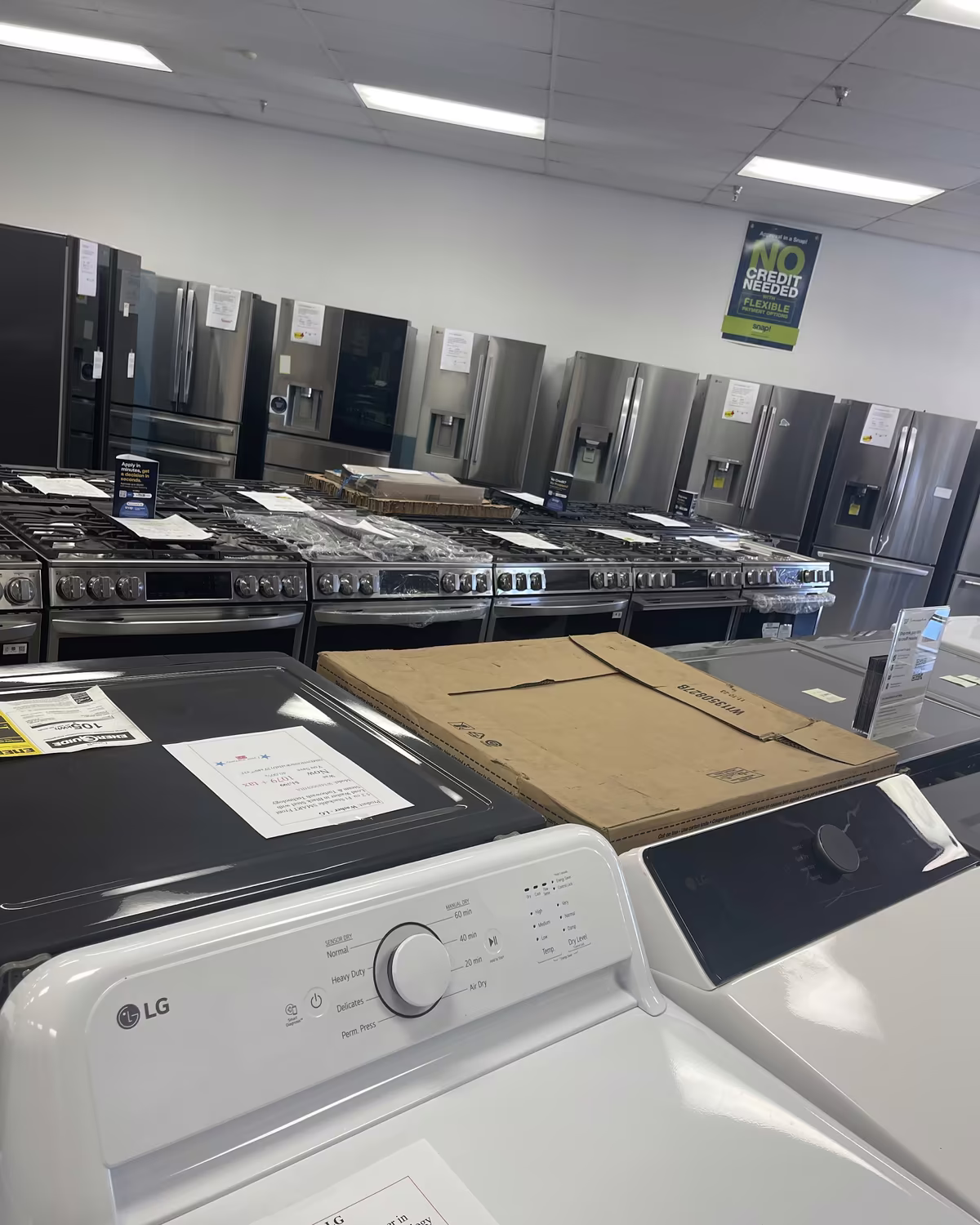 An LG top-load washer in front of rows of ranges and refrigerators